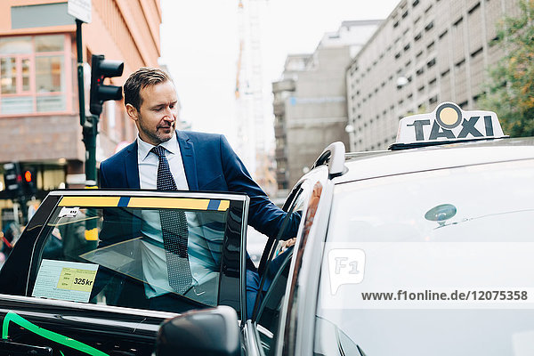 Mature businessman entering taxi in city