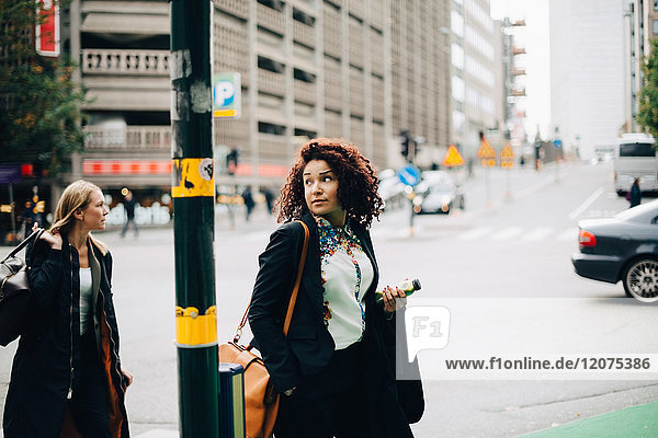 Female business colleagues walking by pole in city