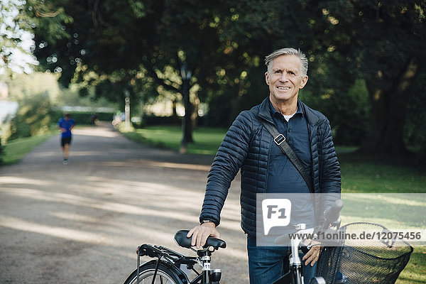 Portrait of smiling senior man with bicycle standing in park