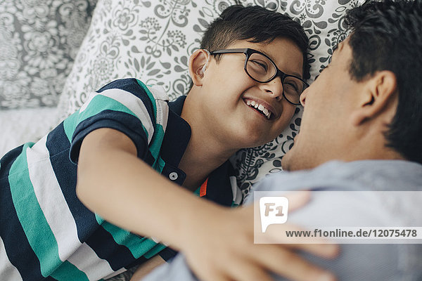 Happy disabled boy looking at father while lying on bed at home
