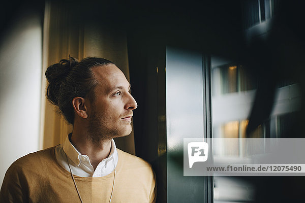 Thoughtful businessman looking through window standing at office