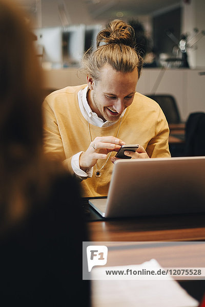 Lächelnder Geschäftsmann mit Smartphone vor einer Kollegin im Büro
