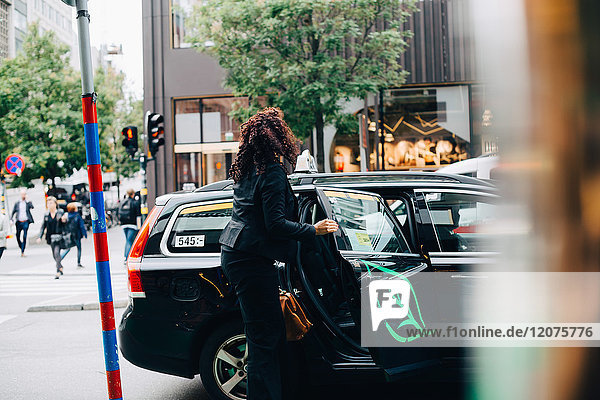 Mittlere erwachsene Geschäftsfrau  die in ein Taxi auf der Straße in der Stadt einsteigt.