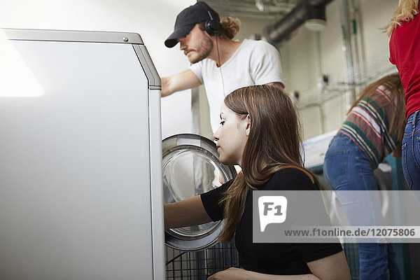 Young male and female friends doing laundry at laundromat