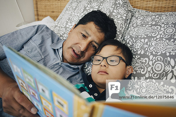 Father reading book to son while lying on bed at home