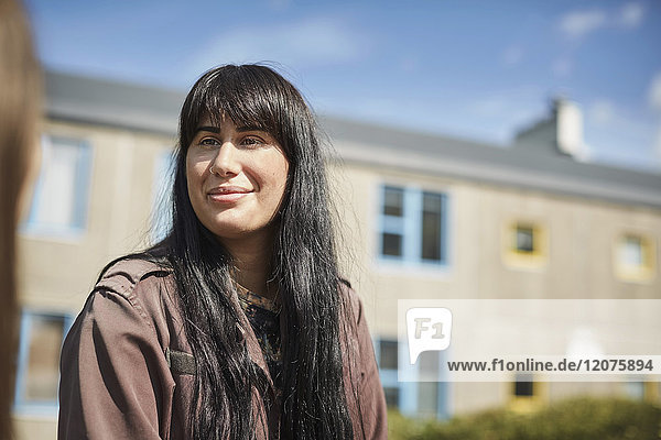 Lächelnde junge Frau mit langen schwarzen Haaren auf dem Uni-Campus