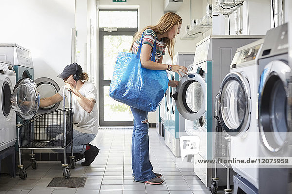 Volle Länge der männlichen und weiblichen Universitätsstudenten beim Wäschewaschen im Waschsalon