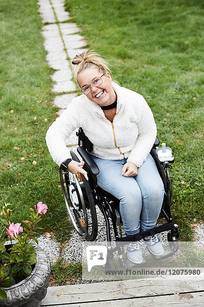 Ganzflächiges Porträt einer lächelnden behinderten Frau  die auf einem Rollstuhl im Hinterhof sitzt.