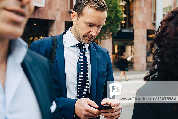 Reife Geschäftsleute mit Smartphone  die hinter Kollegen in der Stadt stehen.