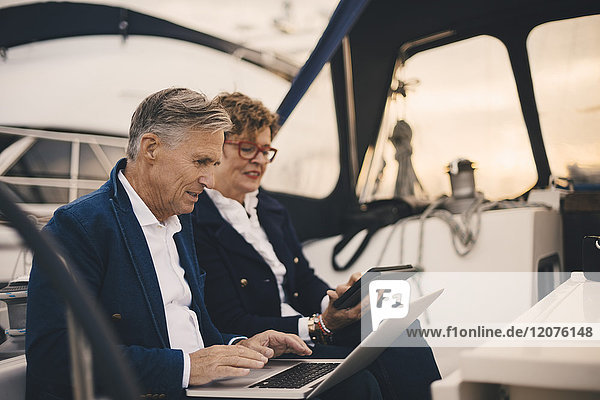 Seniorenpaar  das bei Sonnenuntergang in der Yacht unterwegs ist und Technologien einsetzt
