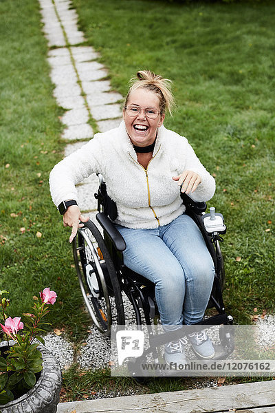 Ganzflächiges Porträt einer lächelnden behinderten Frau auf dem Rollstuhl im Hof