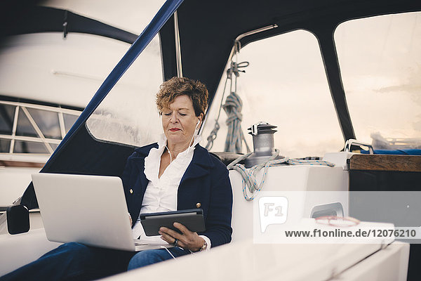 Seniorin mit digitalem Tablett und Laptop in der Yacht