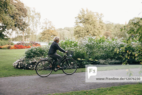 Full length of senior woman riding bicycle in park