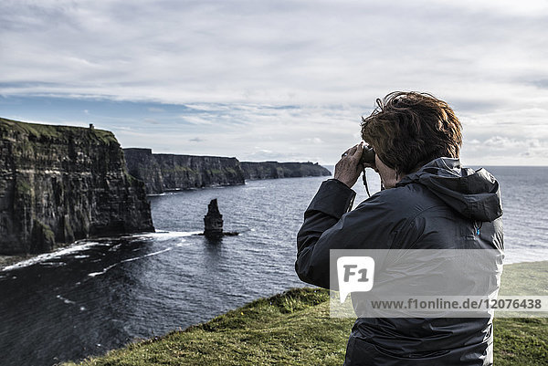 Irland  Grafschaft Clare  Frau schaut durch ein Fernglas auf die Cliffs of Moher