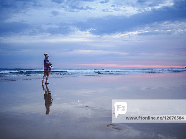 Australien  New South Wales  Frau steht in der Abenddämmerung am Strand