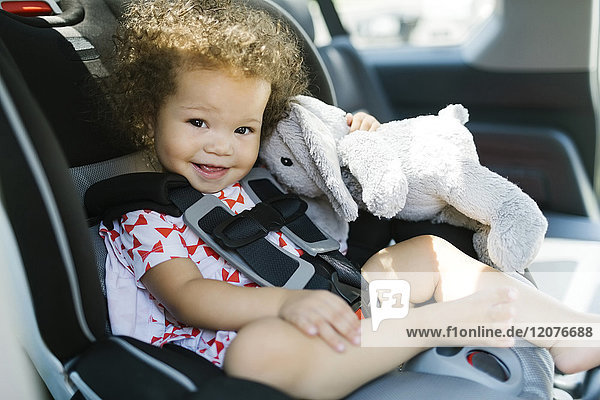 Girl (12-17) sitting on car seat and holding plush toy