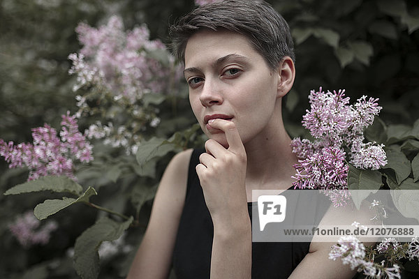 Curious Caucasian woman near flowering tree with finger on lip