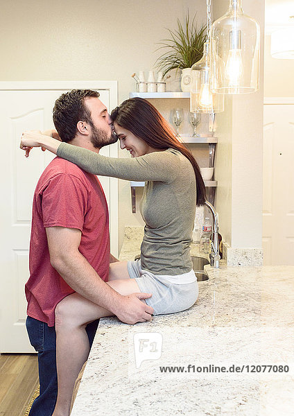 Kaukasischer Mann küsst die Stirn einer Frau in der Küche