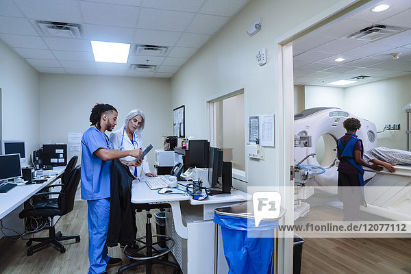 Arzt und Krankenschwester diskutieren über ein digitales Tablet in der Nähe eines Scanners