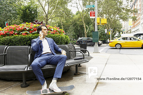 Caucasian businessman sitting on bench in city talking on cell phone