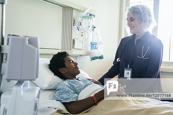 Doctor comforting boy in hospital bed holding cell phone