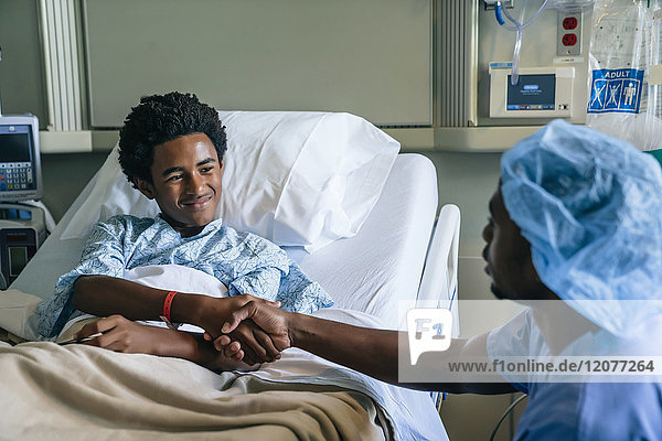 Black nurse shaking hands with boy in hospital bed