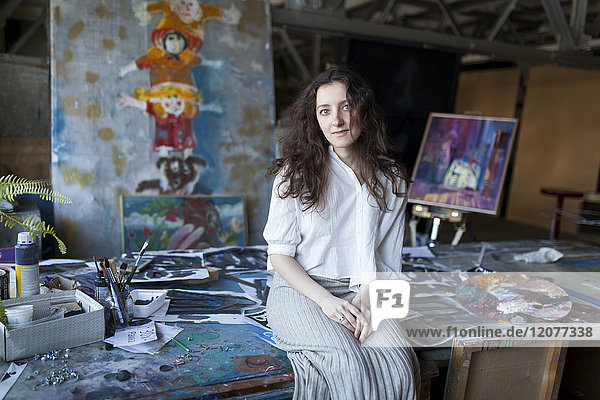 Caucasian artist sitting on table in studio
