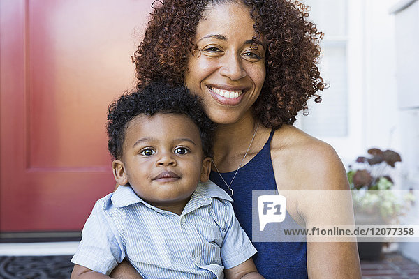 Lächelnde gemischtrassige Mutter und ihr kleiner Sohn sitzen auf der Treppe