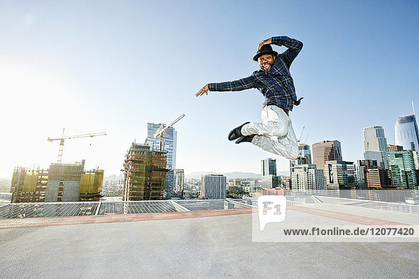 Schwarzer Mann tanzt und springt auf dem Dach einer Stadt