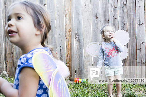Curious girls wearing fairy wings in backyard