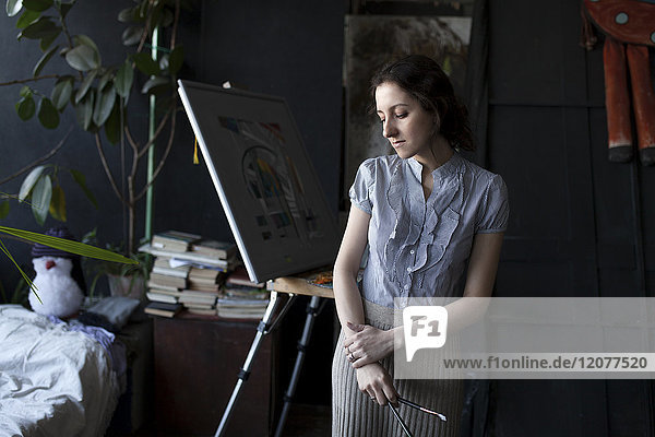 Pensive Caucasian artist holding paintbrushes
