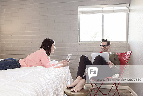 Caucasian couple using digital tablet and laptop in bedroom