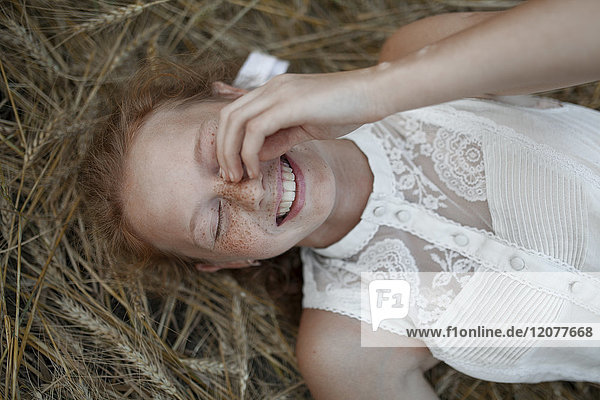 Lächelndes kaukasisches Mädchen mit Sommersprossen liegt im Weizen