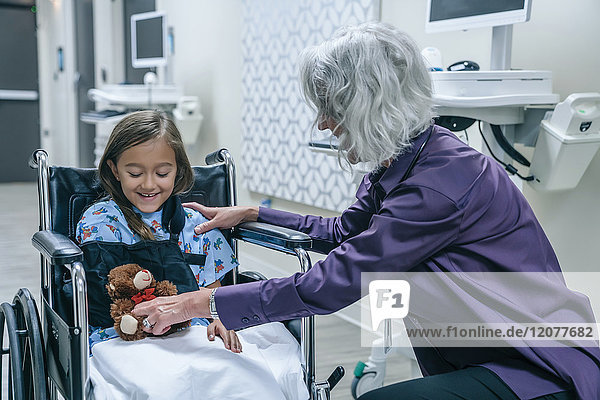 Doctor giving teddy bear to girl in wheelchair