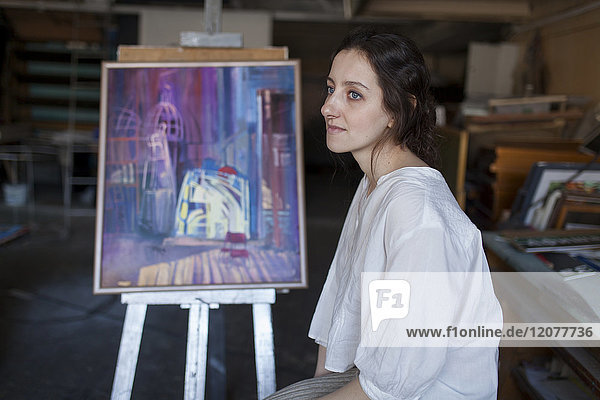 Caucasian artist sitting near paintings