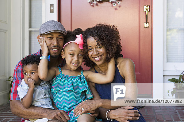 Portrait of smiling mixed race family sitting on front stoop