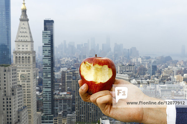 Hand of Caucasian man holding bitten apple on urban rooftop