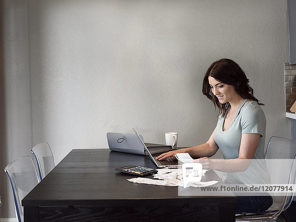 Caucasian woman holding receipt and using laptop