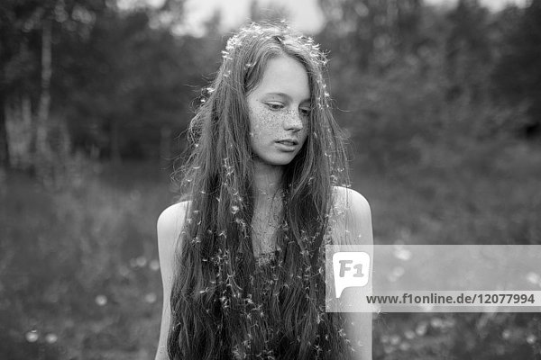 Caucasian girl standing in field with fuzz in hair