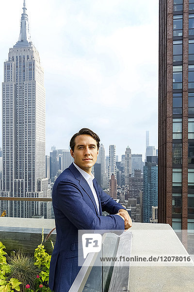 Portrait of serious Caucasian businessman leaning on urban rooftop