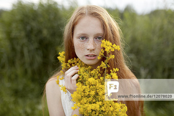 Portrait of serious Caucasian girl with freckles holding wildflowers