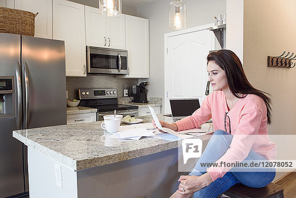 Caucasian woman reading paperwork in kitchen