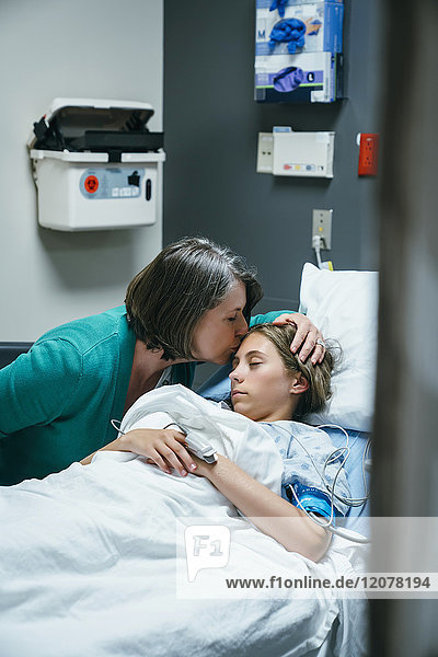 Mutter küsst die Stirn ihrer Tochter im Krankenhausbett