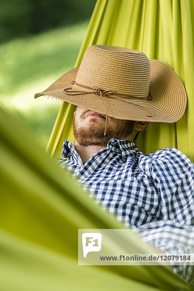 Mann entspannt in der Hängematte mit Hut im Gesicht
