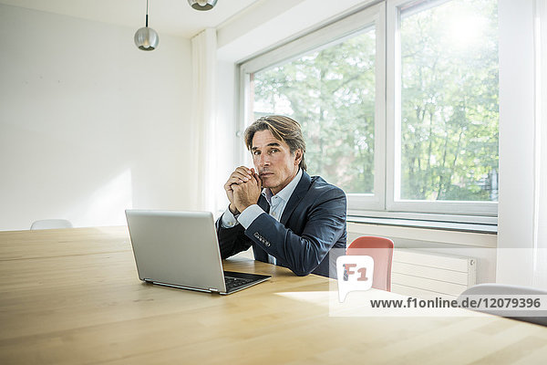 Portrait eines Geschäftsmannes mit Laptop am Tisch im Büro