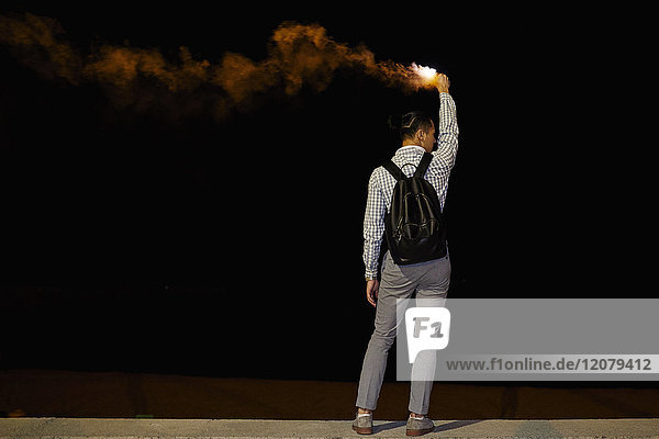 Rückansicht des Mannes mit Rucksack und Flamme bei Nacht