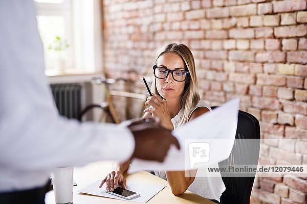 Colleague showing paper to serious woman at desk in office
