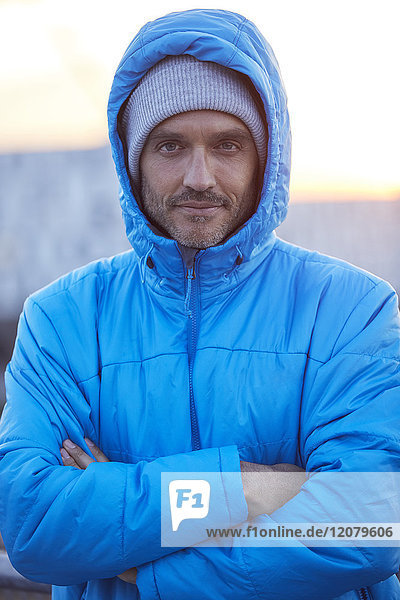 Portrait of confident man with hooded jacket and wooly hat in the city