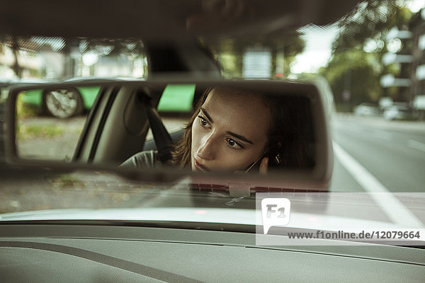 Spiegelbild der jungen Frau im Auto beim Telefonieren