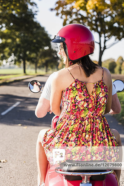 Young couple riding motor scooter on country road